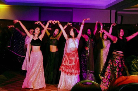 Dancers in lehengas performing on stage under purple lights